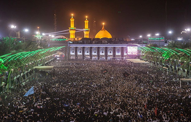 تعداد زیادی از مردم در جوار حرم امام حسین در مراسم مذهبی اربعین حسینی با انواع پرچم سبز رنگ 